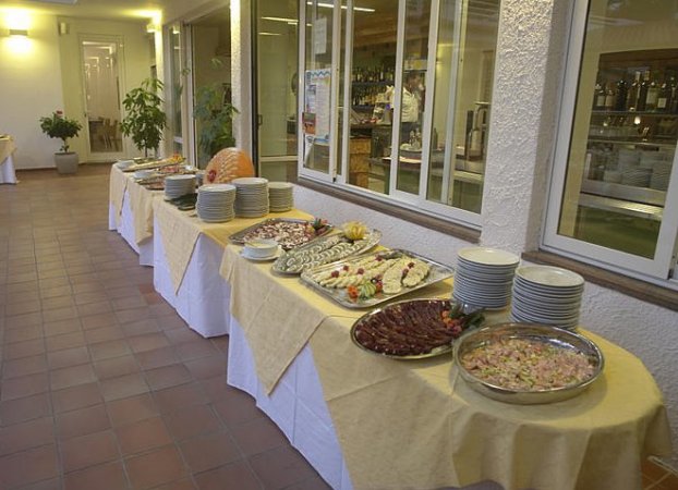 Buffet con vari piatti su tavoli, piatti impilati ai lati.