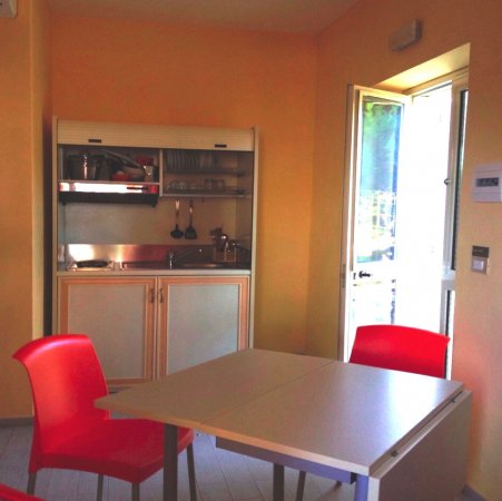 Interno moderno con due sedie rosse e tavolo quadrato. Porta aperta e piccolo angolo cottura.