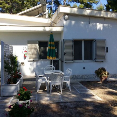 Terrazza esterna con tavolo e sedie bianche. Ombrellone verde e giallo e piante in vaso.