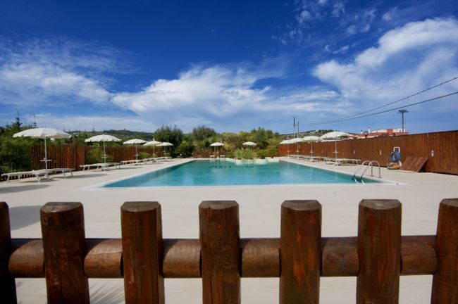 Piscina con ombrelloni bianchi, recinzione di legno.