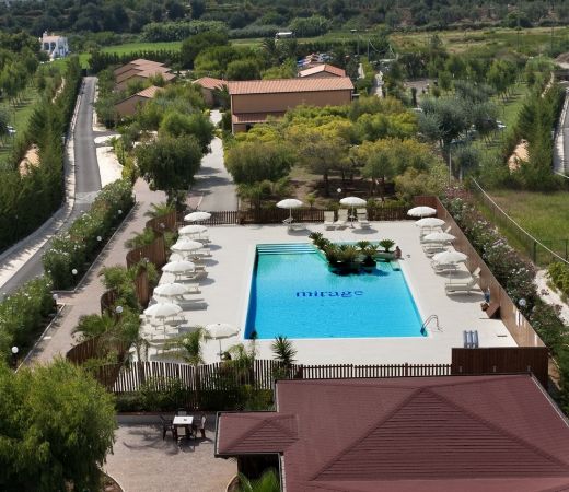 Vista dall'alto di una piscina con ombrelloni e vegetazione.
