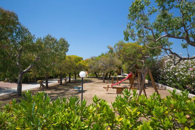 Area giochi in un parco alberato con un'altalena e uno scivolo.