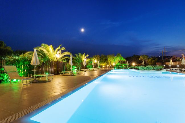 Piscina illuminata di notte con palme.