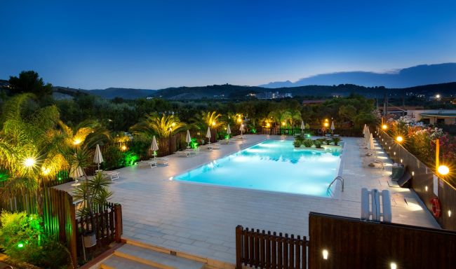 Piscina con luci notturne, circondata da palme.