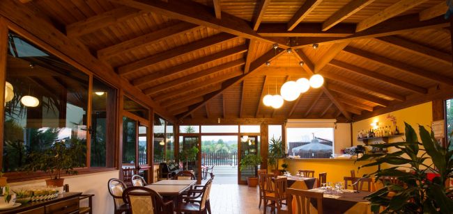 Sala da pranzo luminosa con tavoli e sedie in legno.