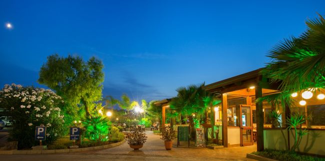 Esterno illuminato di un bar e giardino fiorito di sera.