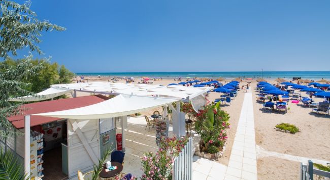 Spiaggia con ombrelloni blu e chiosco a sinistra.
