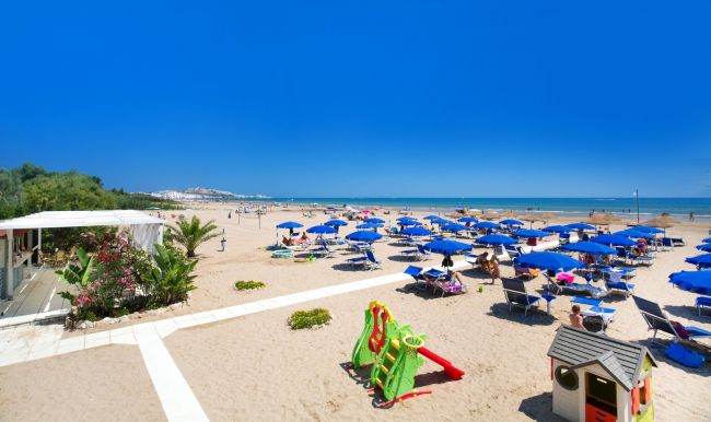 Spiaggia con ombrelloni blu e scivolo verde in primo piano.