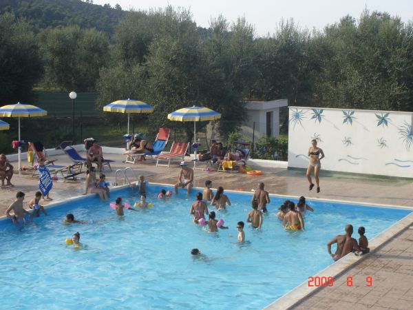 Una piscina all'aperto affollata, circondata da lettini e ombrelloni gialli e blu.
