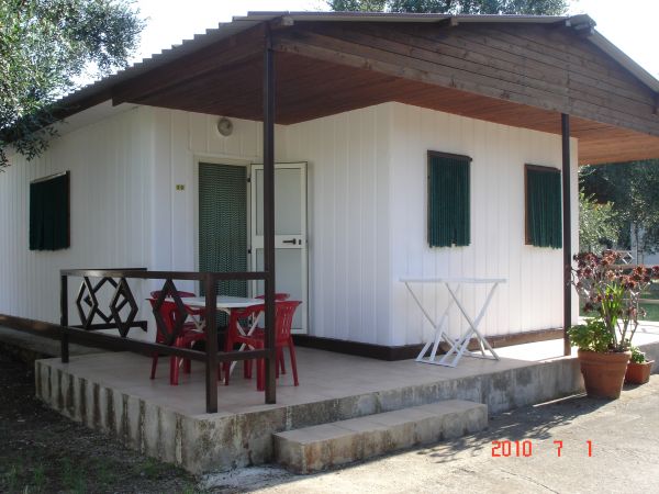 Bungalow bianco con tetto in legno, veranda con tavolo e sedie rosse.