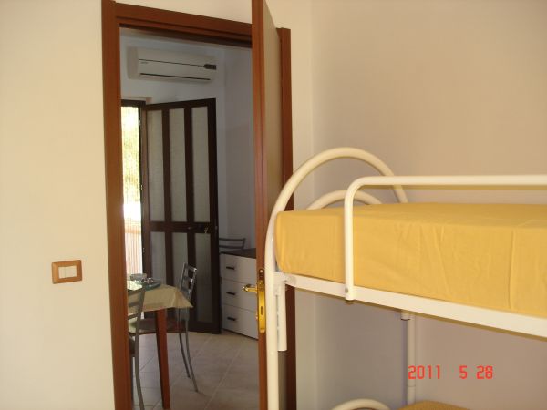 Stanza con letto a castello giallo, porta aperta verso una sala da pranzo con tavolo apparecchiato.