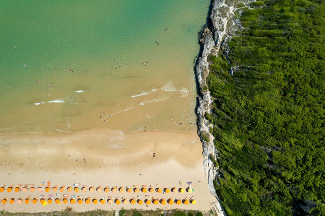 Spiaggia vista dall'alto con ombrelloni arancioni e mare.