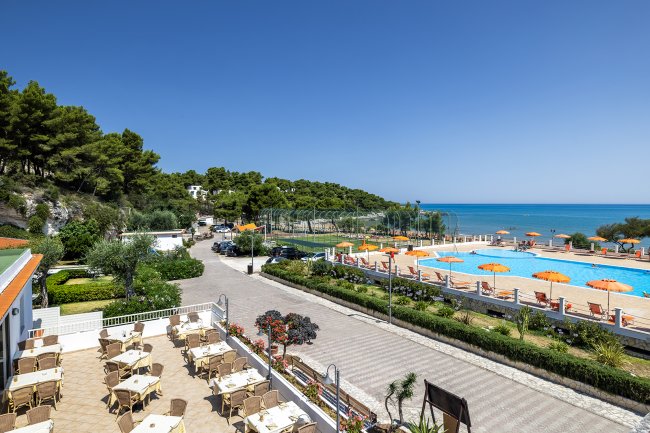 Vista di una piscina con ombrelloni arancioni e tavoli all'aperto vicino al mare.