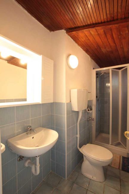 Un bagno con lavabo, toilette e doccia. Pareti piastrellate e soffitto in legno.