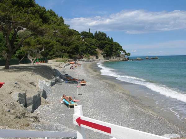 Spiaggia di ciottoli con lettini e mare calmo.