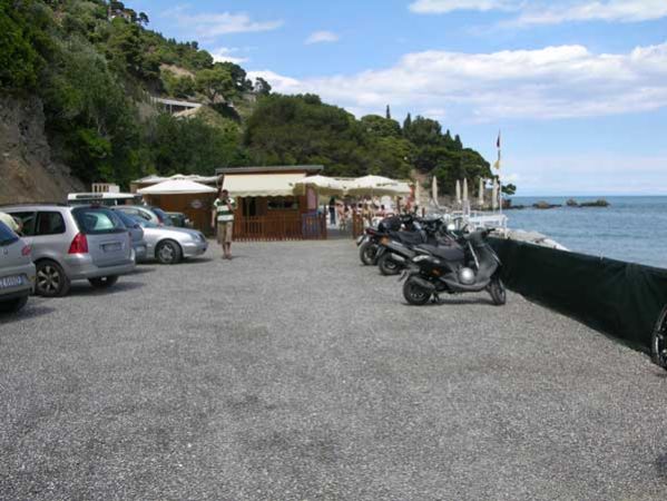 Un parcheggio con auto e scooter vicino al mare.