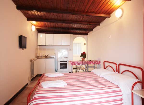 Monolocale con letto matrimoniale a righe rosse, cucina e tavolo. Decorazioni luminose.