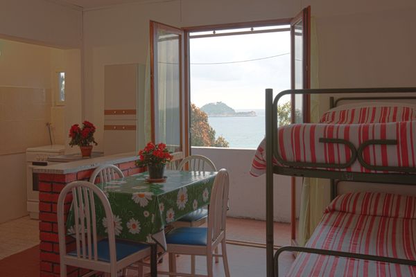 Interno con tavolo e letti a castello, vista mare dalla finestra aperta.