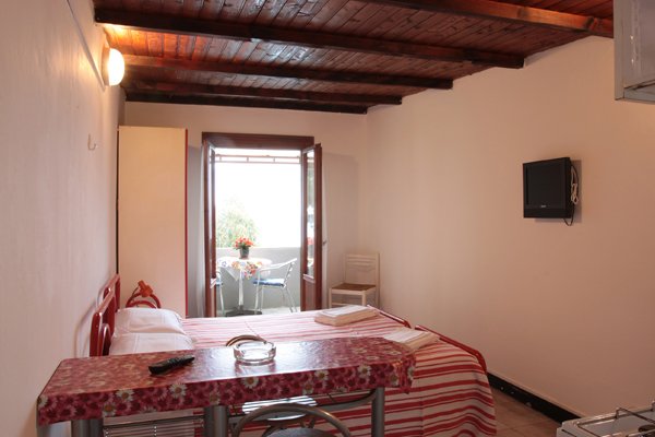 Camera con letto matrimoniale, televisore e porta verso un balcone.