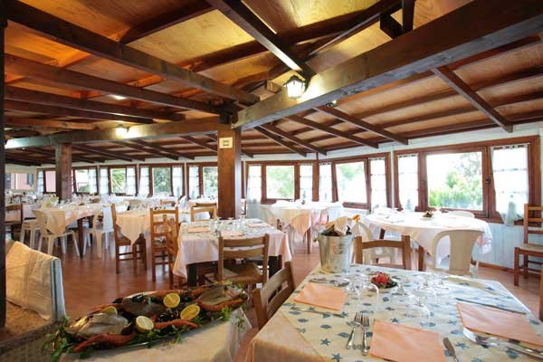 Ristorante con tavoli apparecchiati e piatti decorati, grandi finestre luminose.