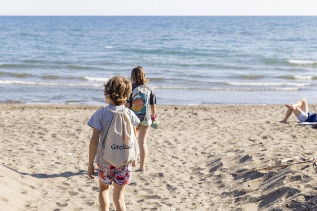 Due bambini camminano verso il mare su una spiaggia.