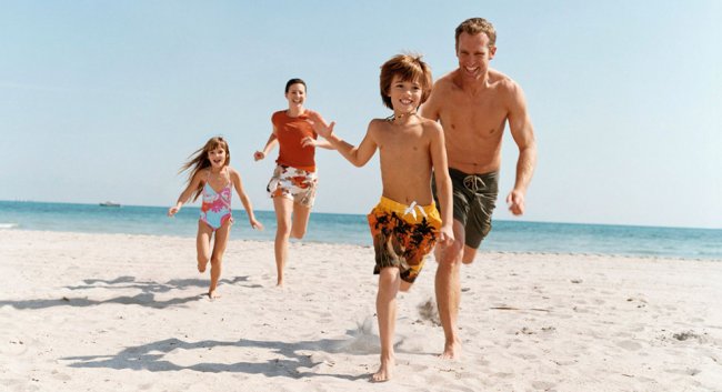 Famiglia corre sorridente sulla spiaggia di sabbia.