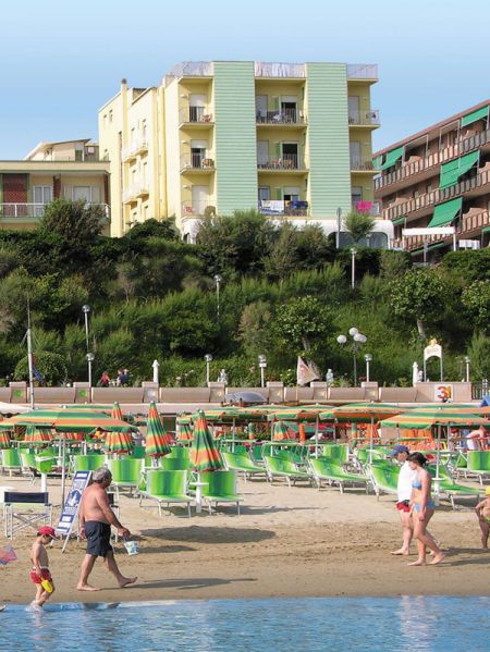 Una spiaggia con ombrelloni verdi e arancioni e un hotel sullo sfondo.