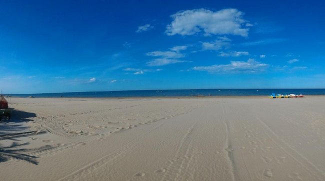 Spiaggia sabbiosa con mare e cielo blu.
