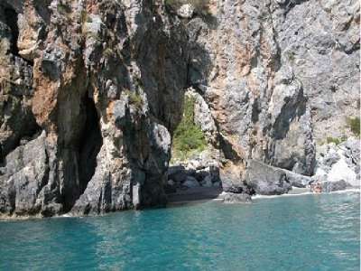 Formazione rocciosa ad arco sulla costa con mare blu al di sotto.