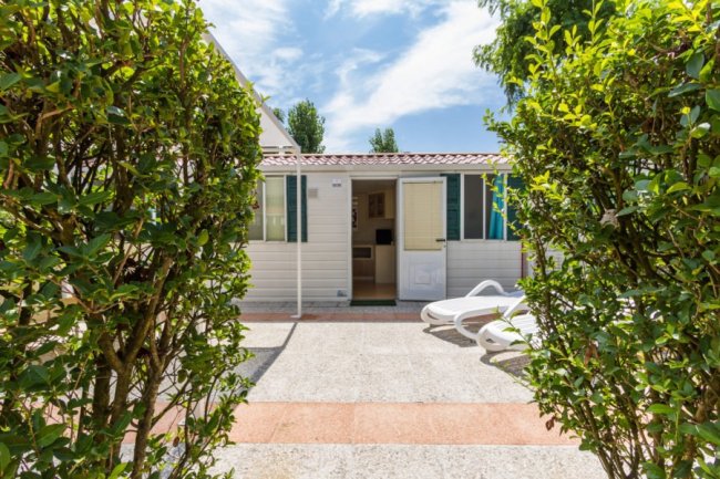 Ingresso di una casa mobile fra siepi, con sedie a sdraio.
