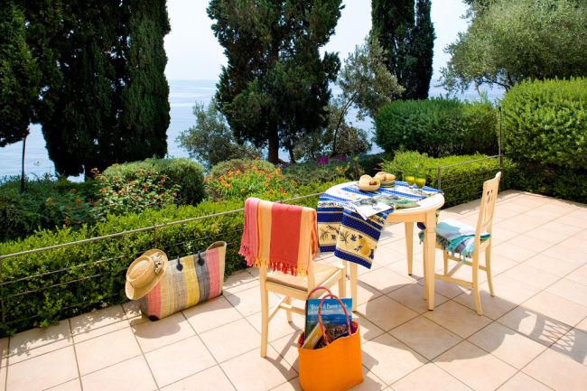 Tavolo su terrazza, alberi e mare sullo sfondo.