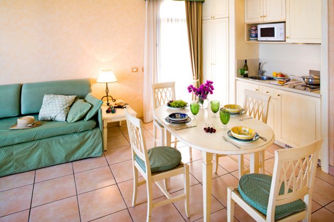 Sala con cucina, tavolo e quattro sedie, divano verde.