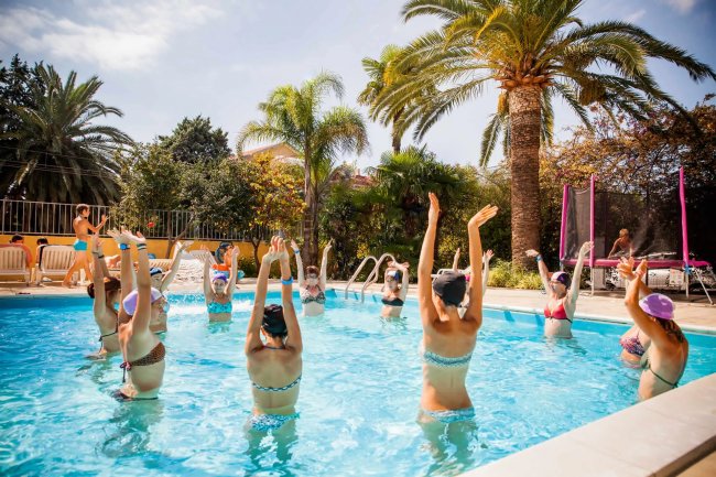 Persone fanno ginnastica in piscina sotto le palme.