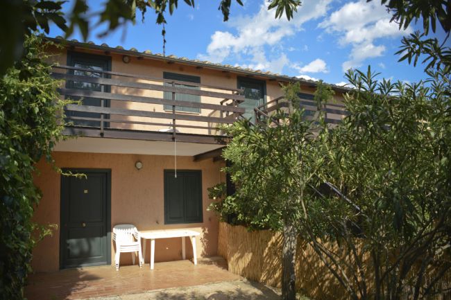Facciata di un edificio con balcone in legno, vegetazione e tavolo esterno.