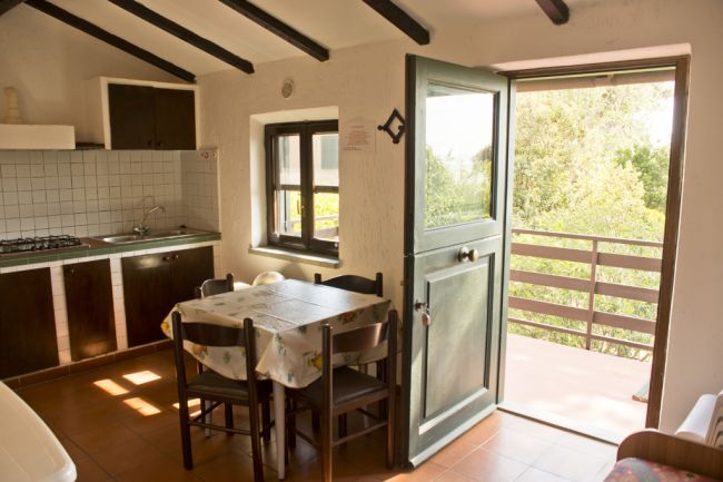 Cucina rustica con tavolo rettangolare e porta aperta su balcone.