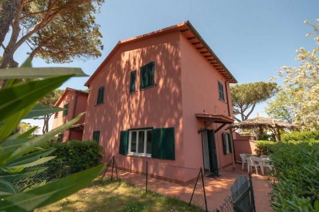 Casa rosa con giardino e alberi intorno.