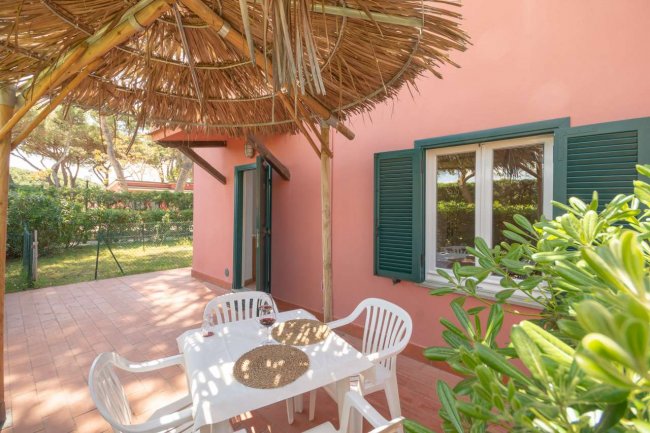 Terrazza con tavolo, sedie bianche e tetto di paglia.