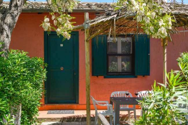 Esterno rosa con tavolo, sedie e pergola fiorita.