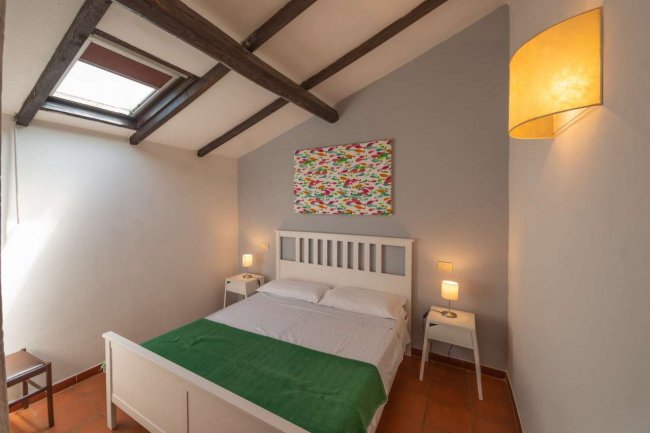 Camera da letto con finestra, letto bianco e travi in legno.