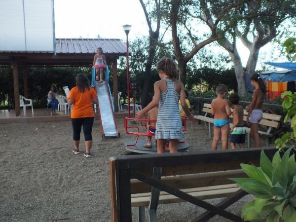 Parco giochi con bambini che giocano su una giostra e uno scivolo.