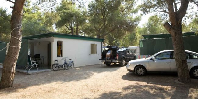 Un bungalow bianco con auto parcheggiate e biciclette fuori.
