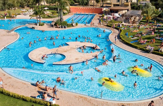 Piscina con numerosi bagnanti e area verde intorno.
