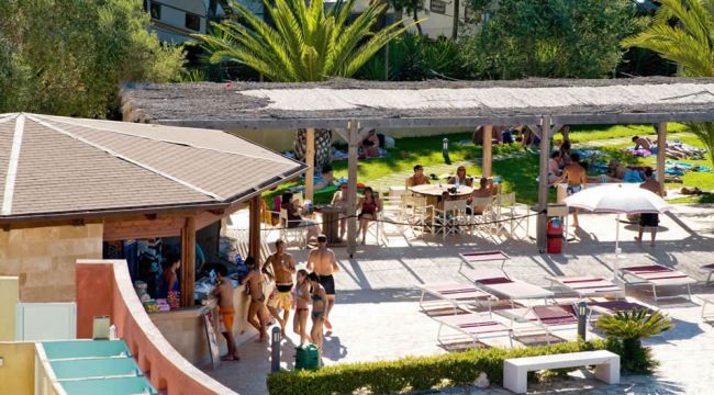 Persone vicino a un chiosco all'aperto, con ombrelloni e lettini.