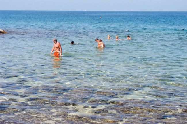 Persone che nuotano in mare limpido con fondo roccioso.