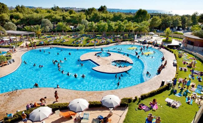 Una piscina affollata circondata da prati e lettini.