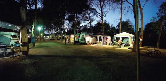 Campeggio notturno illuminato con roulotte e tende.