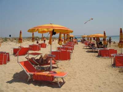 Una spiaggia con ombrelloni arancioni e lettini. Persone rilassate sotto il sole. Atmosfera estiva.