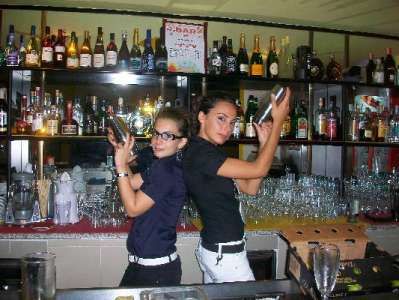 Due baristi al bancone con shaker, circondati da bottiglie.