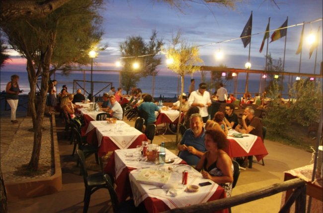 Cena all'aperto al tramonto, con tavoli apparecchiati e persone che conversano.