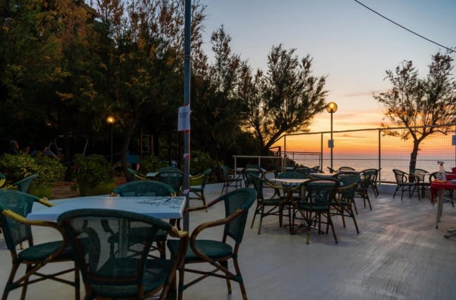 Terrazza all'aperto al tramonto, tavoli vuoti e alberi sullo sfondo.